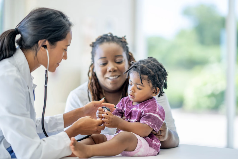 A photo of a mother, daughter and a doctor; the girl is holding the end of the doctor's stethoscope