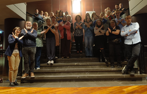 A photo of members of FraXI standing on stairs in the shape of an X and making an X symbol with their arms