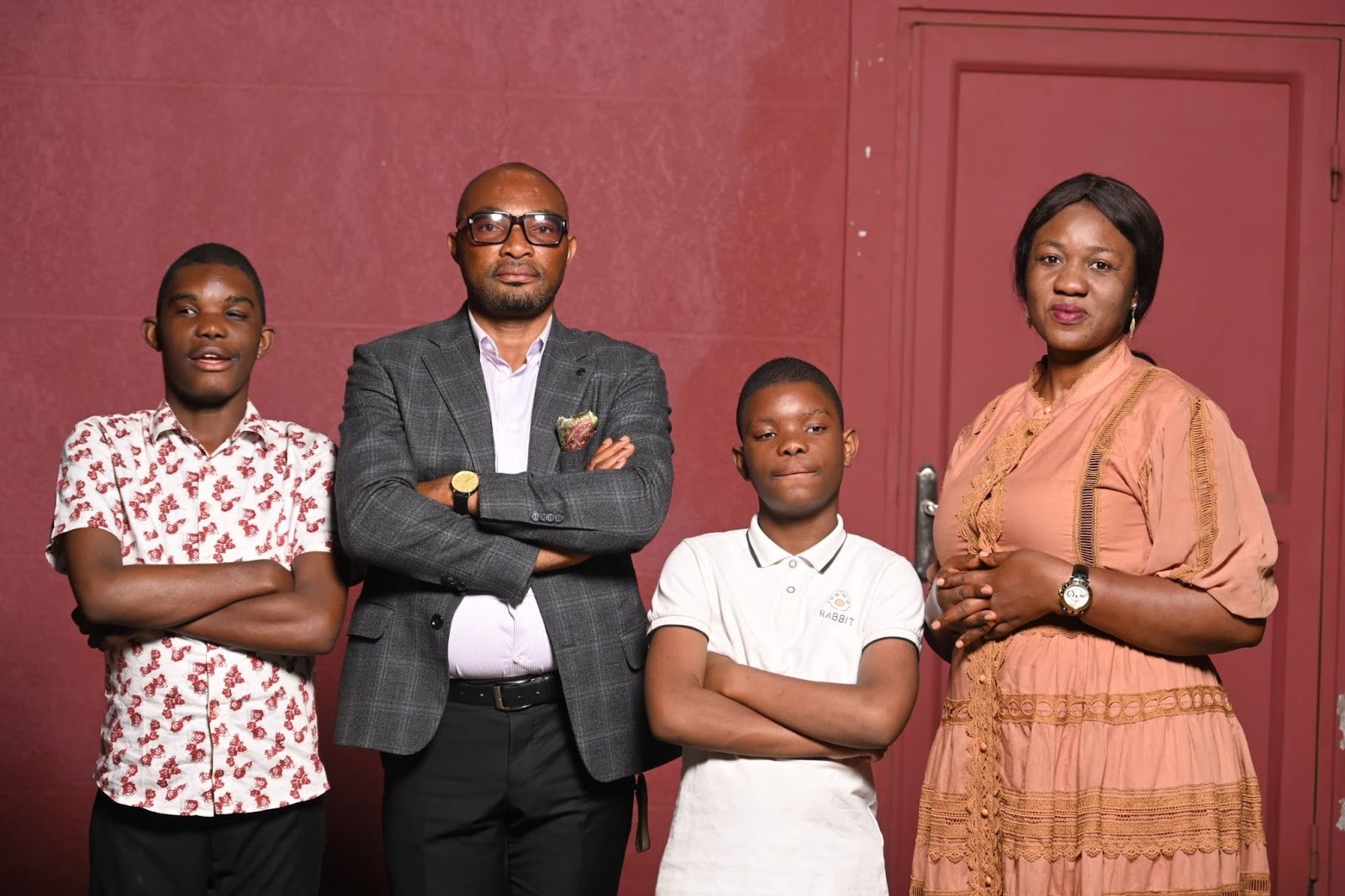 Paulin Madia and Ruth Kabengele with their two boys in front of a red wall