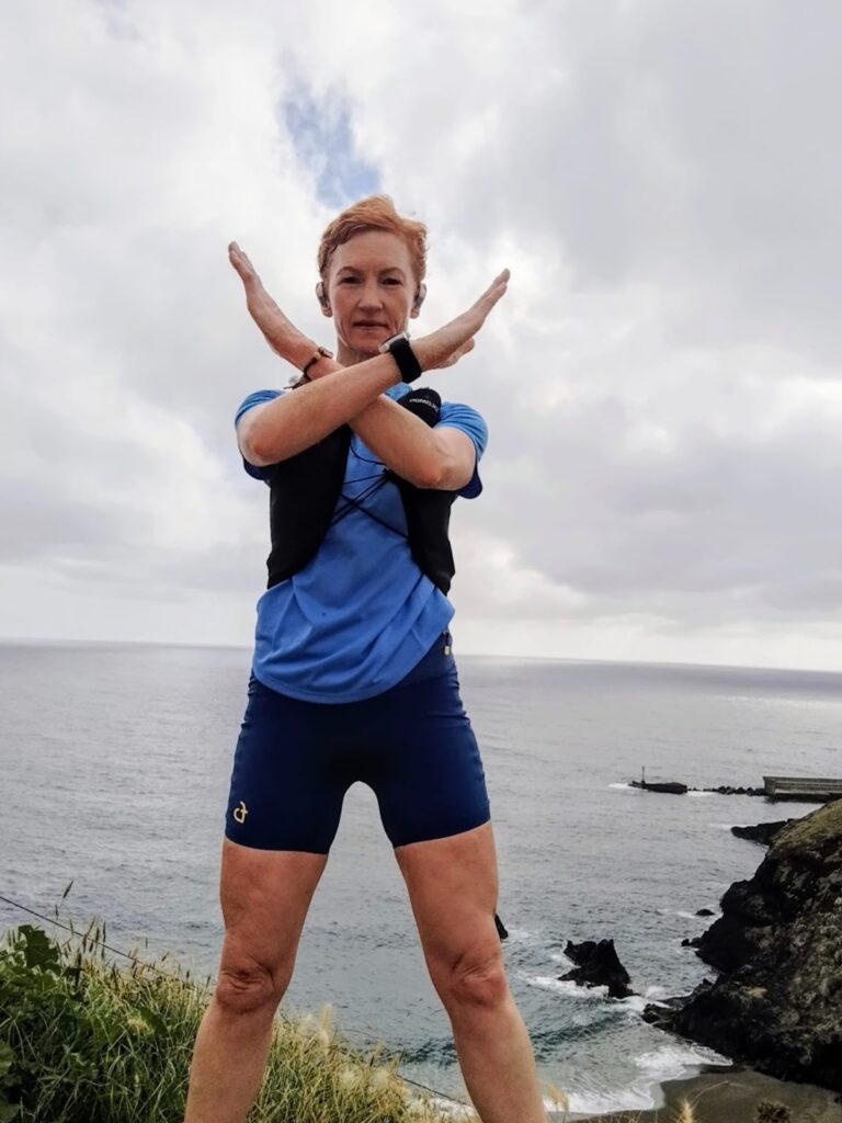 Brid standing in front of the sea and forming an X with her arms